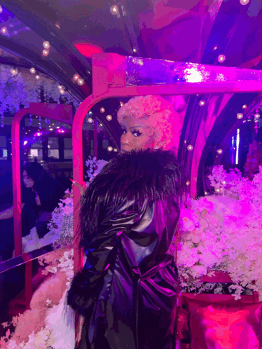 a woman in a black fur coat stands in front of a pink mirror
