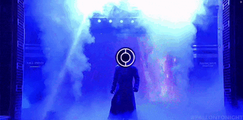 a man in a trench coat is standing in a dark room with smoke coming out of the doorway .