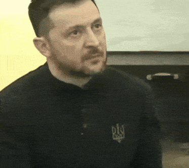 a man with a beard is wearing a black shirt with a symbol on the front