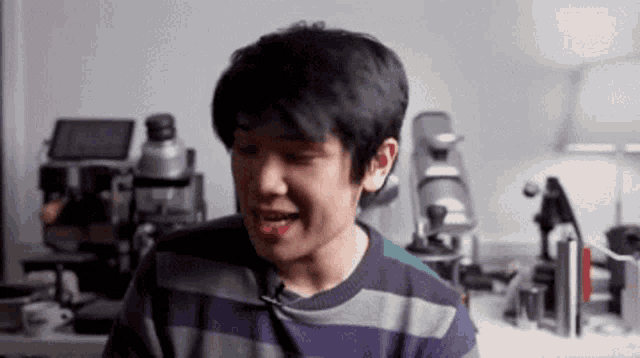 a young man in a striped sweater is making a funny face while sitting at a table .