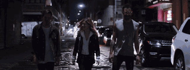 a group of people walking down a street at night with a sign that says ' barber shop ' on it