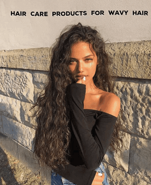 a woman with long wavy hair standing in front of a brick wall
