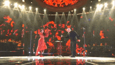 a man and a woman are dancing on a stage with a red background