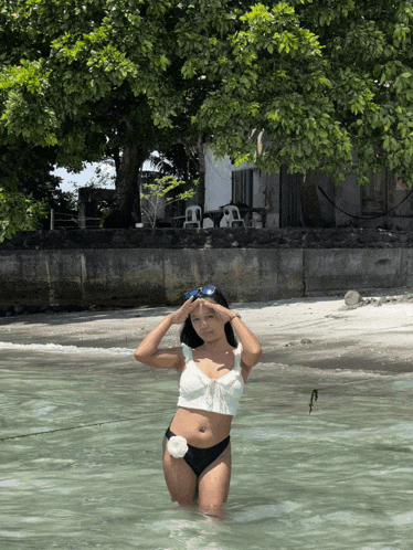 a woman in a bikini is standing in the water with her hands on her head