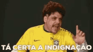 a man in a yellow shirt is pointing at something and the words ta certa a indignacao are above him