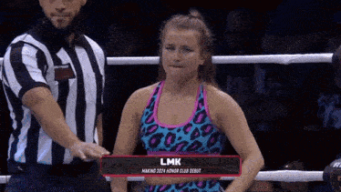 a female boxer named lmk is standing in a boxing ring with a referee .