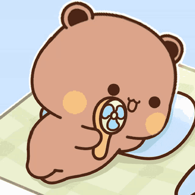 a cartoon bear is laying on a blanket with a fan in his mouth