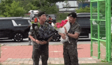 a man in a military uniform holds a bouquet of flowers while standing next to another man