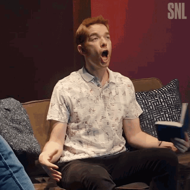 a man is sitting on a couch with his mouth open and a snl logo in the background