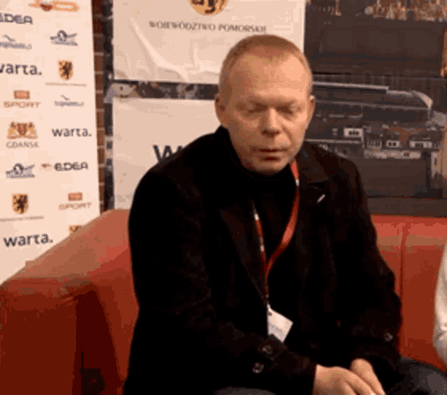 a man sits on a red couch in front of a wall that says warta on it