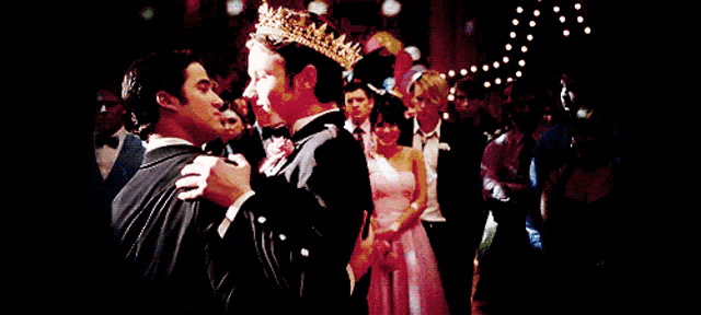 a man in a crown is dancing with another man in a tuxedo