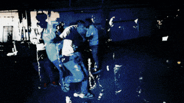 a group of young men are dancing in a room and one of them is wearing a purple sweatshirt