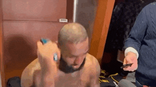 a man without a shirt is shaving his head in a dressing room .