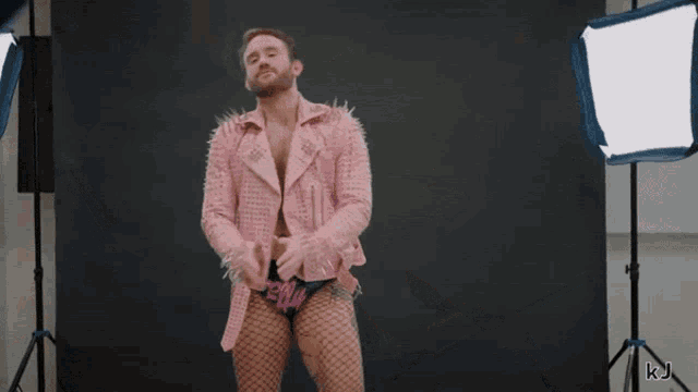 a woman in a pink jacket and fishnet stockings stands in front of a black backdrop with the letters kj on the bottom