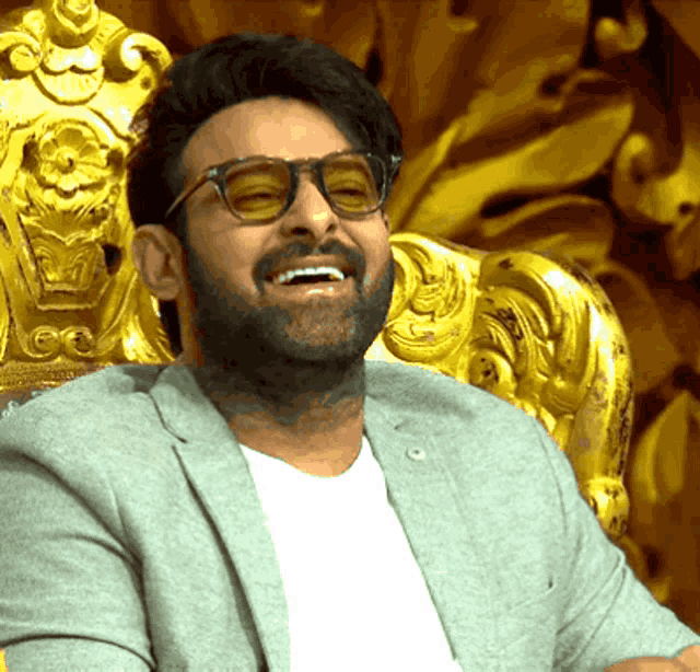 a man wearing sunglasses and a grey jacket is sitting in a chair and smiling