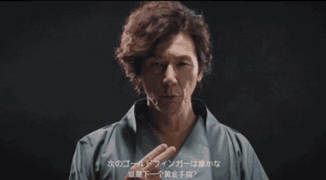 a man in a blue shirt is pointing at the camera with chinese writing on the bottom