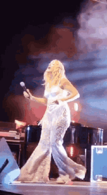 a woman in a white dress is singing into a microphone on a stage