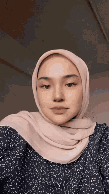 a woman wearing a hijab and a polka dot shirt takes a selfie