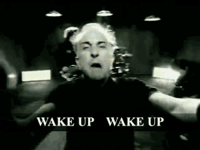 a man is standing in front of a drum set with the words wake up wake up above him .