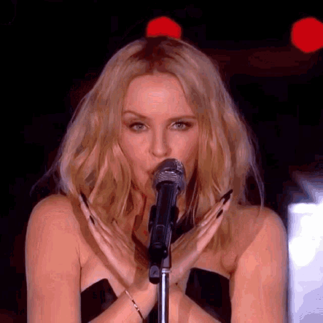 a blonde woman is singing into a microphone with her hands crossed