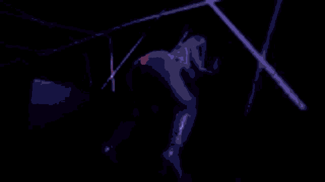 a woman in a latex outfit is dancing in a dark room with purple lights .