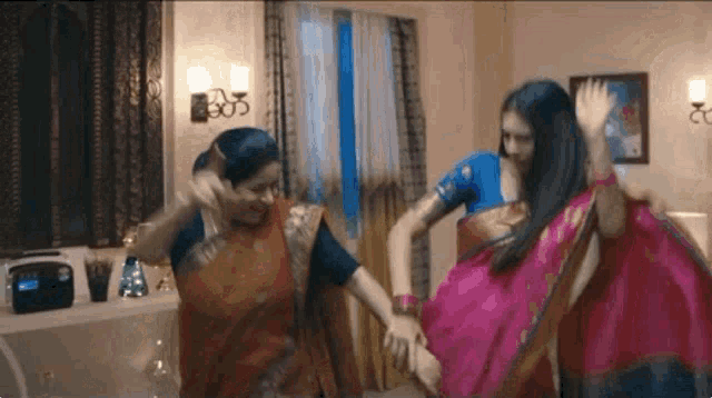 three women in saris are dancing in a room .
