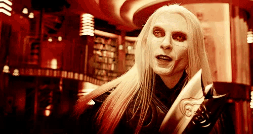 a man with long white hair is holding a knife with a heart on it