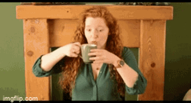 a woman with red hair is drinking from a green cup