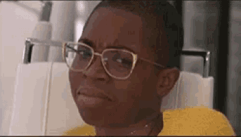 a woman wearing glasses and a yellow shirt is sitting in a chair .