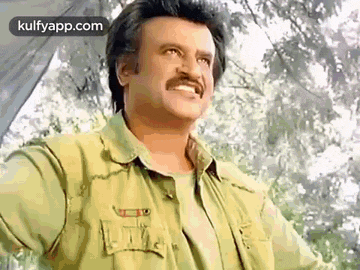 a man with a mustache is wearing a green shirt and smiling while standing in front of trees .