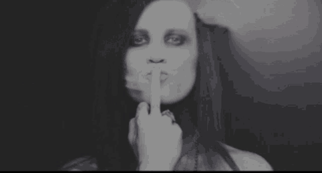 a black and white photo of a woman holding her finger to her mouth .