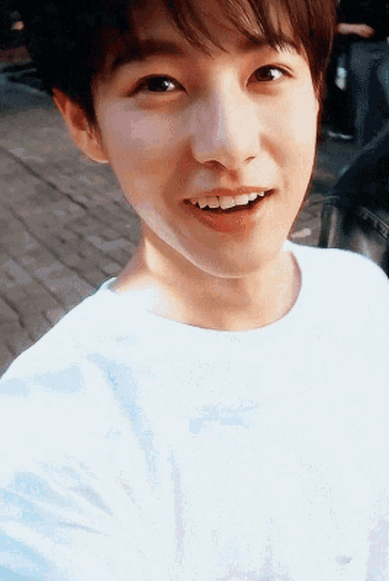 a young man wearing a white shirt is smiling