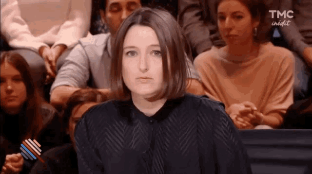 a woman is sitting in front of a crowd of people and making a funny face .