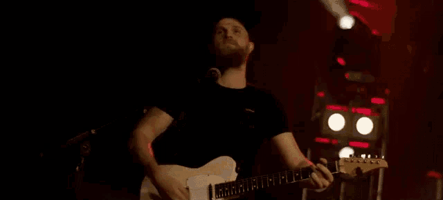 a man with a beard is playing a guitar on a stage in a dark room .