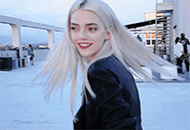 a woman with long blonde hair wearing a black jacket is smiling