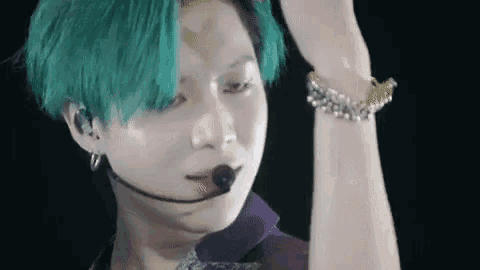 a close up of a person with green hair wearing a microphone and bracelet .