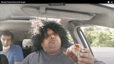 wendy 's pretzel bacon pub burger is being eaten by a man in a car