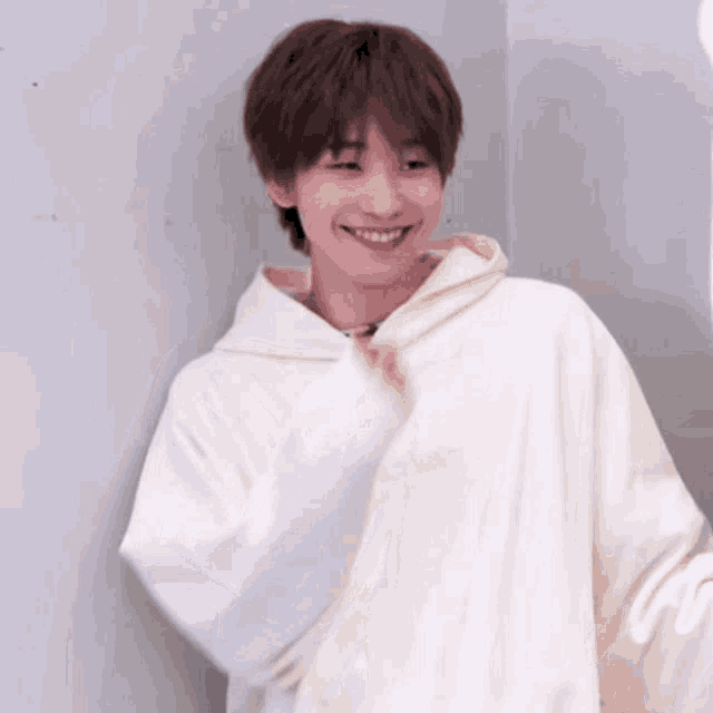 a young man wearing a white hoodie is smiling and looking at the camera .