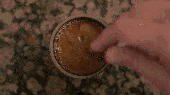 a person is stirring a cup of coffee with a spoon on a counter .