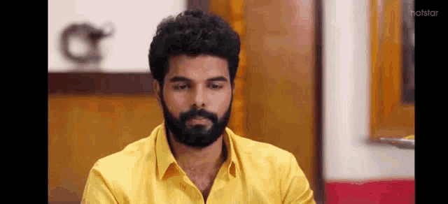 a man with a beard and a yellow shirt is sitting at a table .