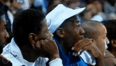 a group of men are sitting in a crowd watching a basketball game . one of the men is wearing a white hat .