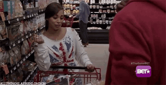 a woman is pushing a shopping cart in a grocery store and talking to a man .