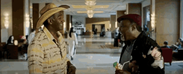 two men in cowboy hats are talking in a lobby