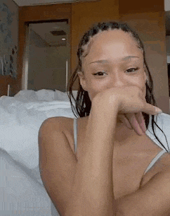 a woman is sitting on a bed with her hand over her mouth .