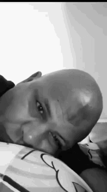 a man with a bald head is laying on a bed with his head on a pillow .