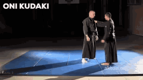 two men are standing on a blue mat with the words oni kudaki behind them