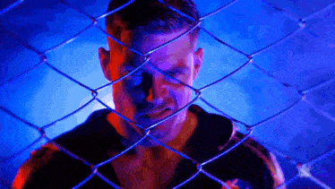 a man is behind a chain link fence with a blue background