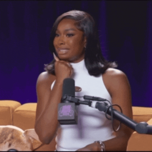 a woman is sitting in front of a microphone with her hand on her chin