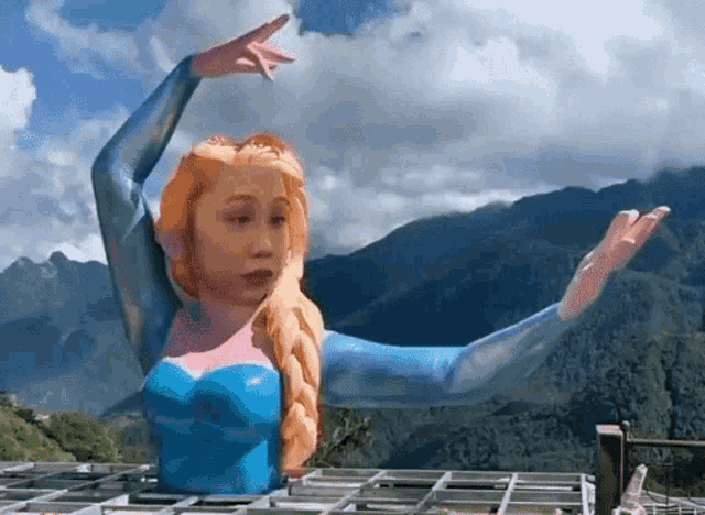 a statue of elsa from frozen with her arms outstretched in front of mountains