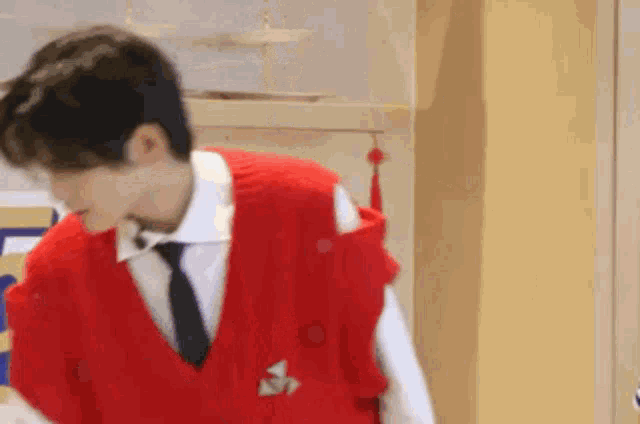 a man wearing a red vest and tie is standing in front of a cabinet .